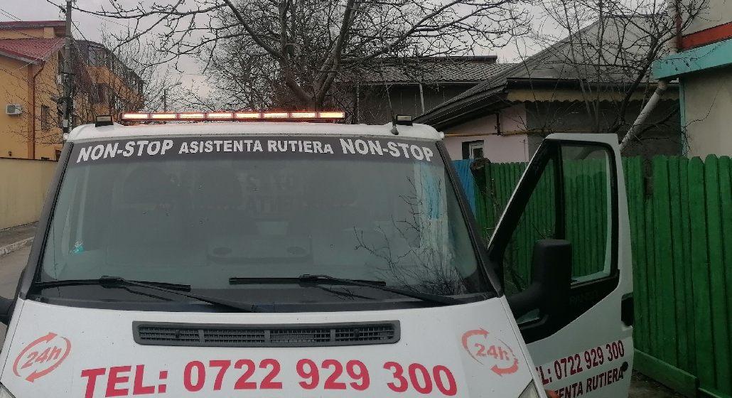 Platformă de tractare cu girofarul aprins și inscripția NON-STOP ASISTENȚĂ RUTIERĂ pe parbriz.