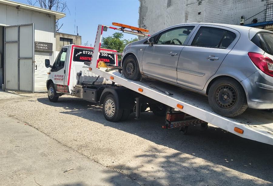 Autoturism urcat pe platformă cu troliul, într-o curte de service.