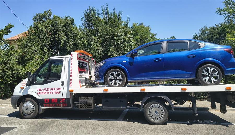 Autoturism nou, transportat pe platformă, parcat într-o parcare marcată.