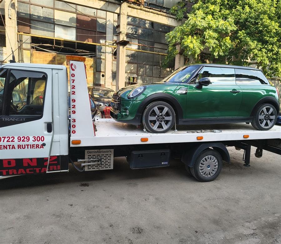 Autoturism compact verde, pe platformă, lângă o hală.